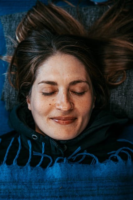A woman laying on the floor covered by a blanket breathing through her nose.