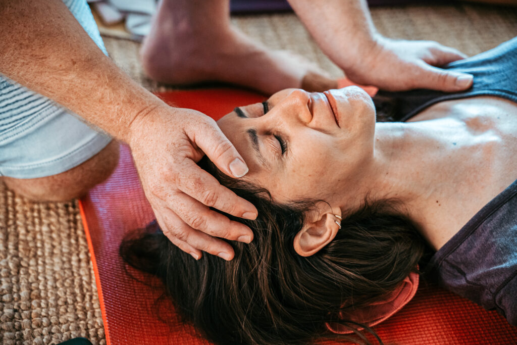 A breathwork instructor with their hands on a student's head.