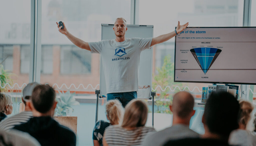 A breathwork facilitator standing in front of a group of students with his hands up.