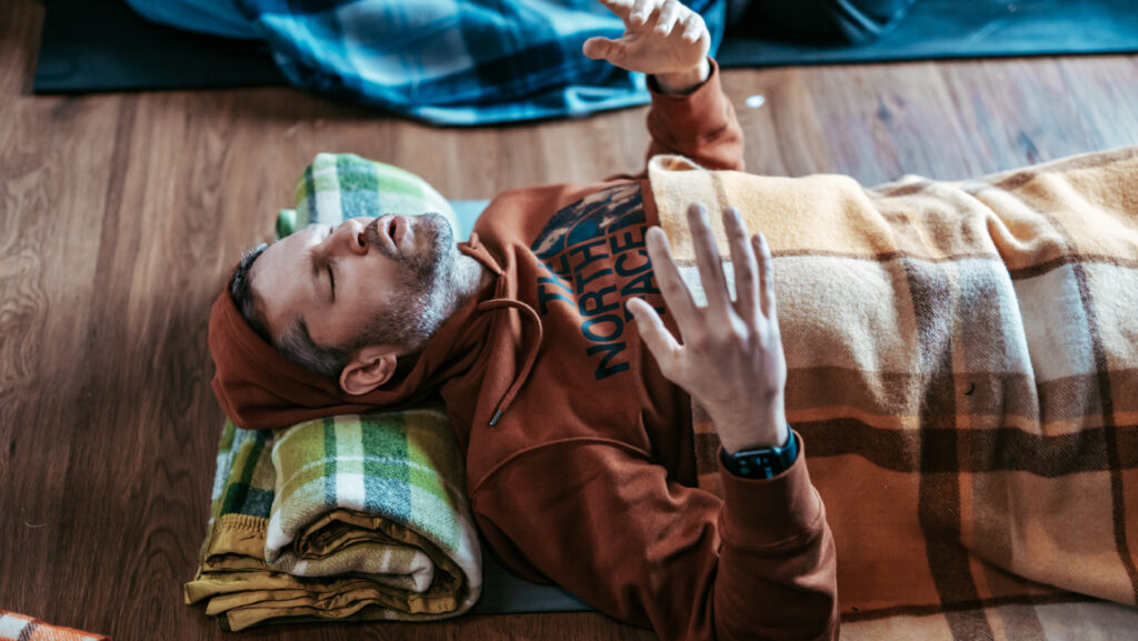 Man laying down and lifting his hands and having a psychedelic breathwork experience.