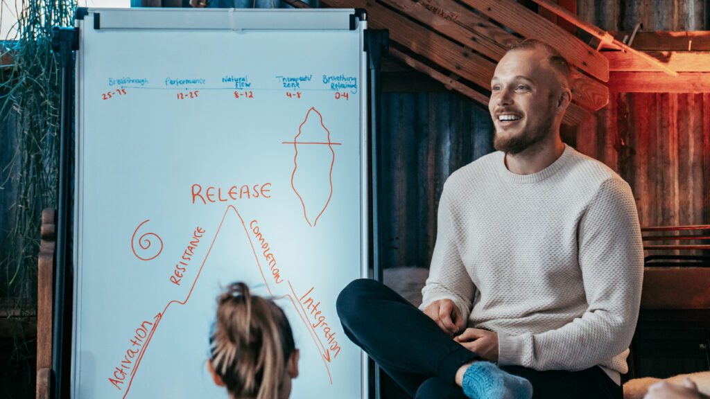 A man sitting in front of a whiteboard that shows the benefits of breathwork on it