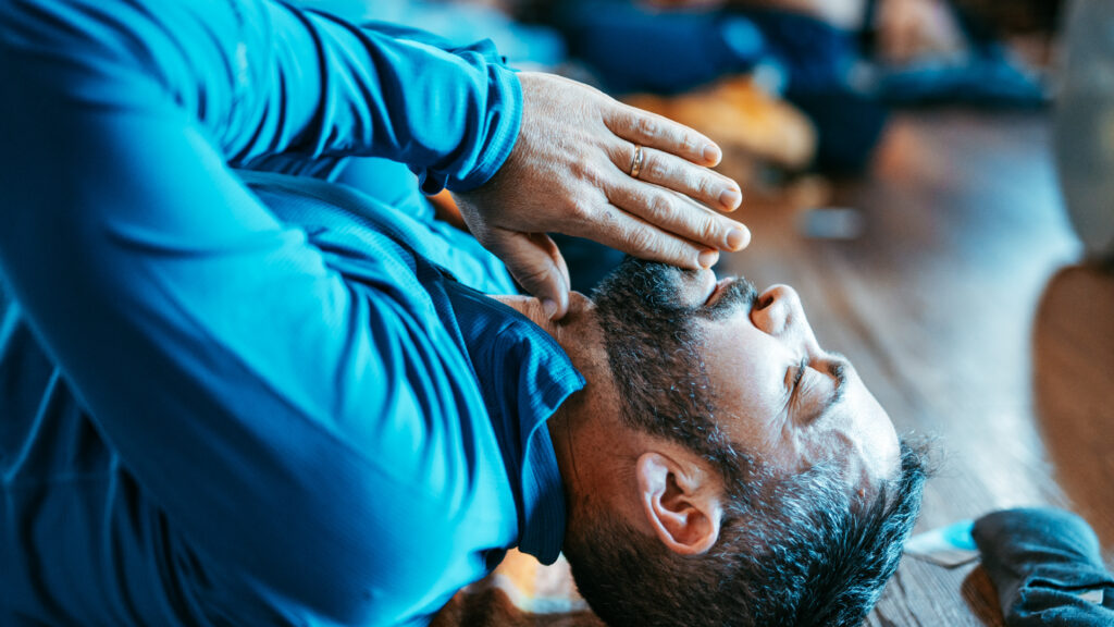 A man lying on the floor with his hands on his face during his breathwork practice.